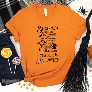 K&ouml;nnte beinhalten: Orangefarbenes T-Shirt mit schwarzem Text, der "Shadows of a thousand years rise again unseen Voices whisper in the trees Tonight is HALLOWEEN" lautet.