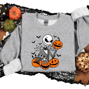 May include: A gray sweatshirt with a black and white illustration of Jack Skellington from The Nightmare Before Christmas holding a pumpkin. The illustration is surrounded by bats and pumpkins.