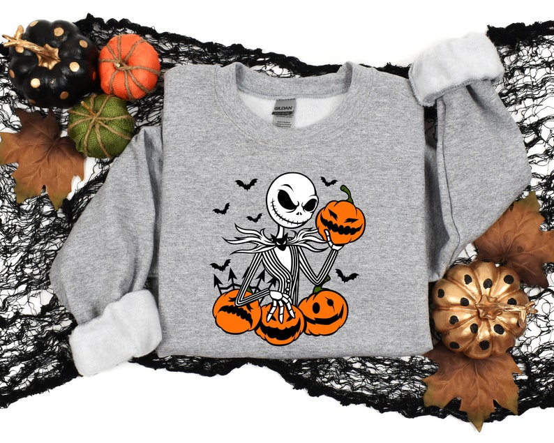 May include: A gray sweatshirt with a black and white illustration of Jack Skellington from The Nightmare Before Christmas holding a pumpkin. The illustration is surrounded by bats and pumpkins.