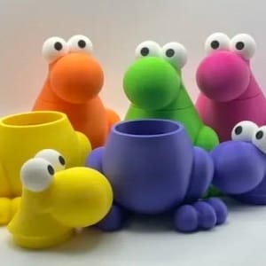 Puede incluir: Una colecci&oacute;n de organizadores de escritorio con forma de rana, coloridos y caprichosos. Los organizadores son de varios colores brillantes, incluyendo amarillo, naranja, verde, rosa y morado. Cada uno tiene ojos grandes y de dibujos animados y una nariz redonda.