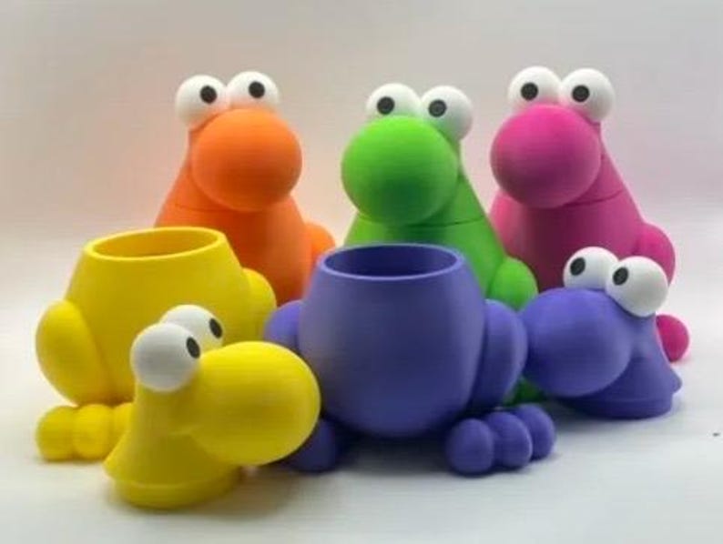Puede incluir: Una colecci&oacute;n de organizadores de escritorio con forma de rana, coloridos y caprichosos. Los organizadores son de varios colores brillantes, incluyendo amarillo, naranja, verde, rosa y morado. Cada uno tiene ojos grandes y de dibujos animados y una nariz redonda.
