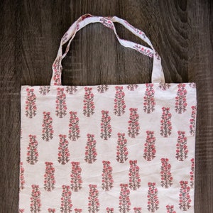 Peut inclure: Sac fourre-tout en coton blanc avec un motif floral répété en rose et gris.