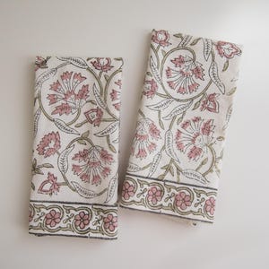May include: Two white cotton tea towels with a pink and green floral pattern. The towels have a border with a repeating floral design.
