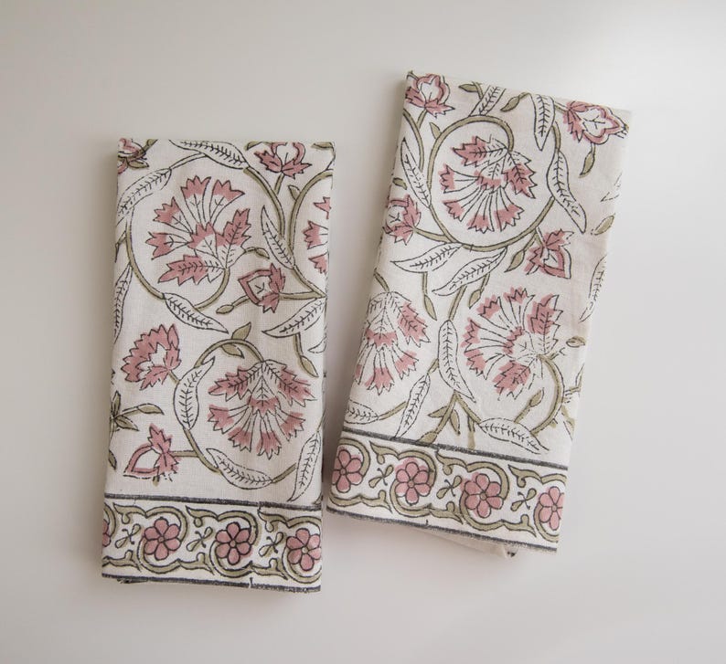 May include: Two white cotton tea towels with a pink and green floral pattern. The towels have a border with a repeating floral design.