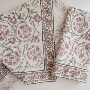 May include: Two white cotton napkins with a pink and green floral print. The napkins have a border of pink and green flowers.