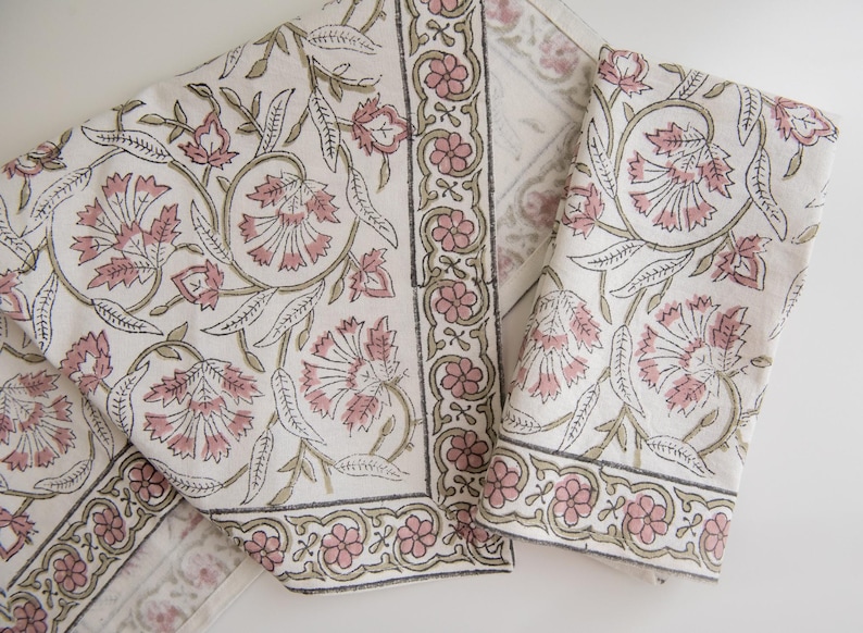 May include: Two white cotton napkins with a pink and green floral print. The napkins have a border of pink and green flowers.
