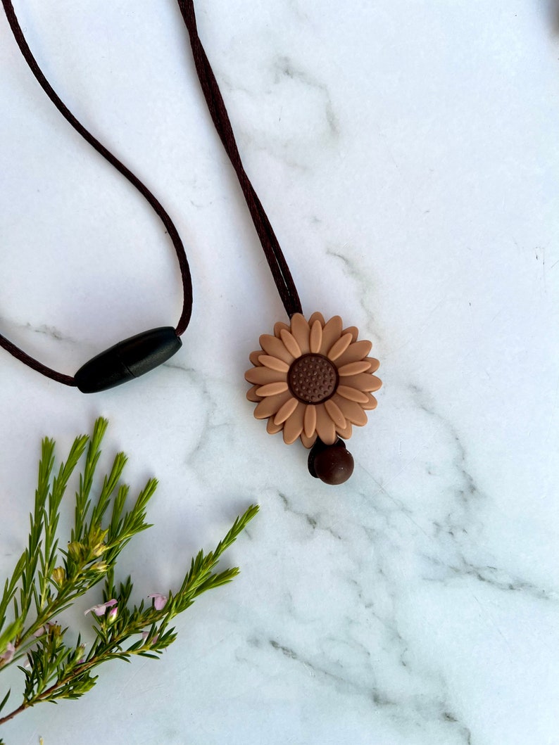 May include: A brown silicone sunflower charm necklace with a brown cord and a black plastic clasp.