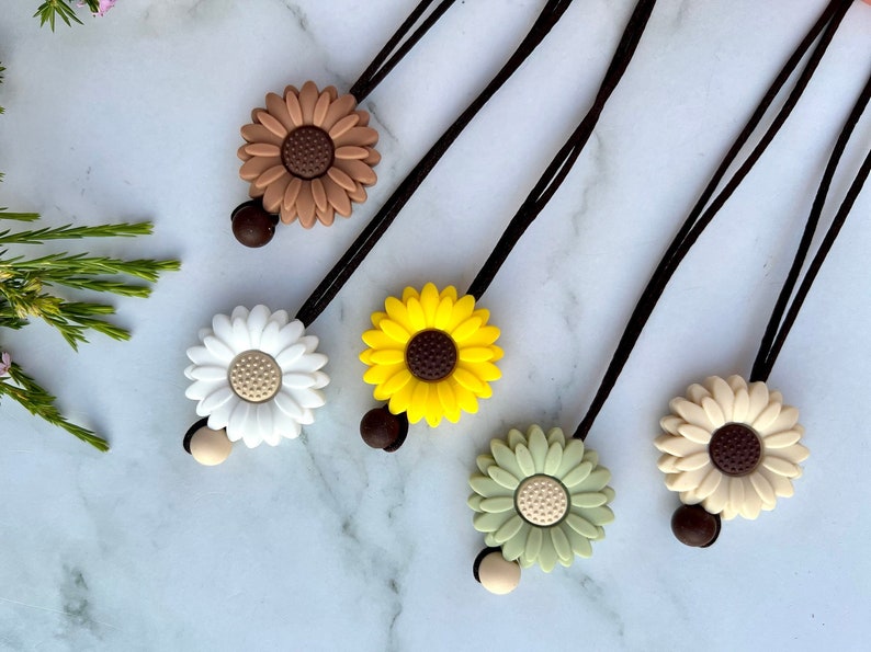 May include: Five colorful flower hair ties with black elastic cords. The flowers are brown, white, yellow, green, and beige.