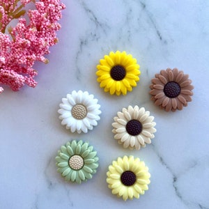 May include: Six small, colorful, silicone sunflower-shaped buttons. The buttons are in shades of yellow, green, brown, and white.