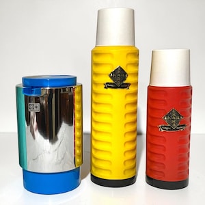 Può includere: Tre thermos vintage e un contenitore. I thermos sono gialli e rossi con coperchi bianchi e basi nere. Il thermos giallo ha un design a coste. Il contenitore è blu, verde acqua e argento. Ogni thermos ha un emblema dorato.