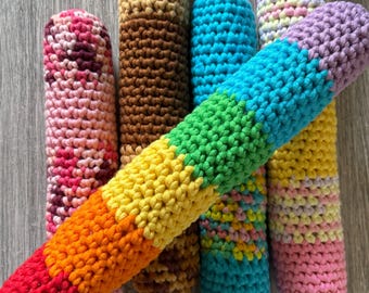 May include: Six crocheted colorful cylindrical toys. The toys are made of different colored yarn and are arranged in a pile. The colors include brown, pink, blue, green, yellow, and orange.