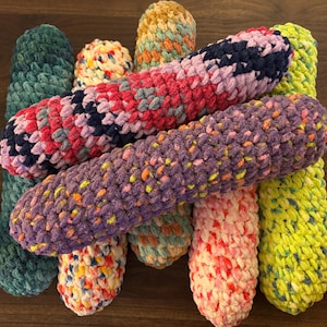 May include: A collection of colorful crocheted yarn rolls in various patterns and colors, including purple, green, pink, and yellow.