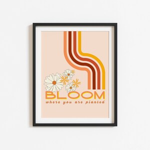 May include: A peach-coloured poster with a retro design featuring a curved line of orange, red and brown stripes. The poster has a white daisy flower design and the text "BLOOM where you are planted".