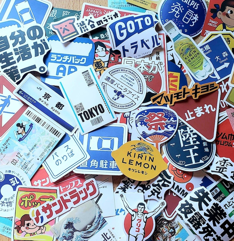 May include: A collection of colorful stickers featuring Japanese text, illustrations, and logos. The stickers include images of a cow, a lemon, a running person, a stop sign, and a building. The stickers are arranged in a random pattern on a surface.