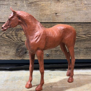 May include: A reddish-brown horse sculpture. The horse is standing with its head up and its legs in a natural stance. The sculpture has a textured surface, giving it a rustic appearance. The horse is a decorative item.