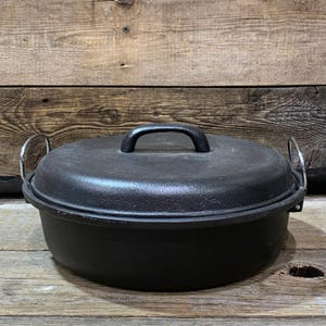 May include: A black cast iron Dutch oven with a lid and two side handles. The lid has a curved handle on top. The pot sits on a wooden surface.