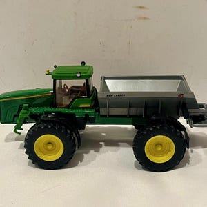 May include: A green and yellow toy tractor with a gray hopper. The tractor has large black tires with yellow centers. The words "NEW LEADER" are printed on the side of the hopper.
