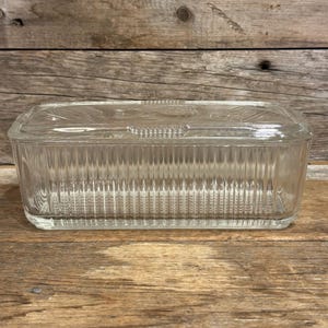 May include: A rectangular clear glass refrigerator dish with a matching lid. The container features vertical ribbing along the sides and a decorative embossed pattern on the top surface of the lid, providing a structured and functional kitchen storage piece.