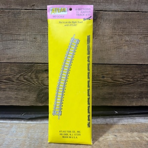 May include: A yellow Atlas HO scale model train track package containing 6 sections of 15 inch radius track. The packaging features black text and a graphic illustration of the curved track, with the Atlas Tool Co. address printed at the bottom.