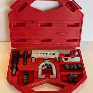 May include: A red plastic toolbox containing various metal automotive tools. The tools include a flaring tool, fittings, and a handle. The toolbox is open, revealing the organized arrangement of the tools.