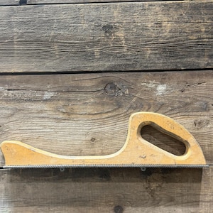 May include: A vintage wooden rasp with a curved handle and a metal file. The rasp is light brown and shows signs of wear, mounted on a weathered wooden surface. The tool is designed for shaping wood.