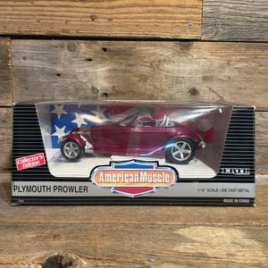 Puede incluir: Un coche a escala 1/18 de metal fundido a presión Plymouth Prowler en color magenta intenso, dentro de una caja negra Collector's Edition con una bandera estadounidense, el logo American Muscle y el texto Made in China.