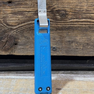 May include: A blue Ideal Industries Inc. wire stripper tool with a silver blade. The tool has a textured handle and a curved blade. The text "IDEAL INDUSTRIES INC. SYCAMORE, ILLINOIS, U.S.A." is printed on the handle.