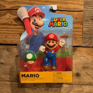 May include: A Super Mario action figure in plastic packaging, featuring a red and blue Mario character with a green 1-up mushroom. The packaging displays the Super Mario logo, the name Mario, and a warning label regarding small parts.