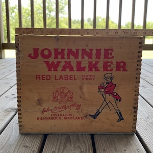 May include: Wooden crate with the words "JOHNNIE WALKER RED LABEL SCOTCH WHISKY" in red lettering. The crate features an illustration of a man in a red coat and top hat. The text "John Walker & Sons, Distillers, Kilmarnock, Scotland" is also visible.