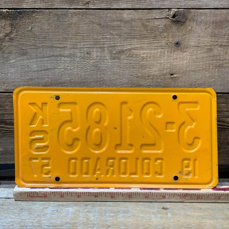 May include: A vintage yellow Colorado license plate with embossed white lettering and numbers. The plate reads "3-ST82" and "COLORADO 81". The plate has four mounting holes and is slightly distressed, showing signs of age.