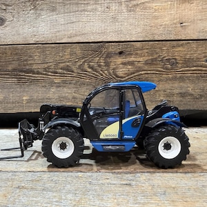 May include: A blue and black toy telehandler with a fork attachment. The model has large black tyres with white rims and a blue cab. The text "LM5060" is visible on the side.