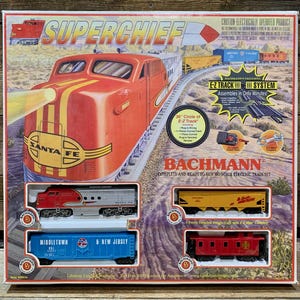 May include: A boxed Bachmann Superchief HO scale electric train set. The box features a red and yellow Santa Fe locomotive. The set includes track and several train cars. The box also states "Assembles in Only Minutes!"