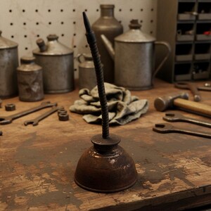 May include: A vintage, rusty oil can with a flexible spout stands on a wooden workbench. Other metal tools and containers are in the background, including wrenches, a hammer, and various cans. The scene evokes a classic workshop aesthetic.