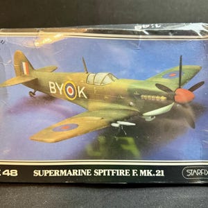 May include: A model kit box featuring a Supermarine Spitfire F. Mk.21 aircraft. The box art shows the olive green and tan plane with the text "BYOK" on the side. The propeller has a red center. The box reads "1:48" and "STARFIX".