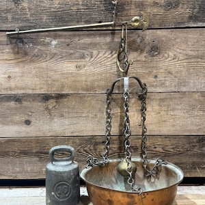 Puede incluir: Balanza antigua de latón colgante con un cuenco de cobre y un peso de hierro fundido. La balanza tiene un brazo largo, cadenas y un gancho para colgar. El cuenco de cobre es redondo. El peso de hierro fundido es gris oscuro.