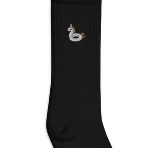 Può includere: Calzini neri fino al polpaccio con un galleggiante per piscina a forma di unicorno bianco ricamato sul davanti.