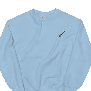 Puede incluir: Una sudadera de color azul claro con una pequeña imagen bordada de una pala de madera en el pecho izquierdo.