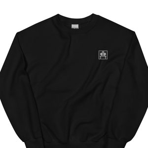 Puede incluir: Sudadera negra con un pequeño logotipo bordado en blanco en el pecho izquierdo. El logotipo es un cuadrado con una imagen estilizada de una persona sentada en una silla.