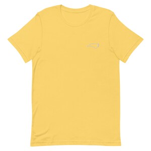 Puede incluir: Una camiseta amarilla de manga corta con un contorno blanco del estado de Carolina del Norte en el pecho izquierdo.
