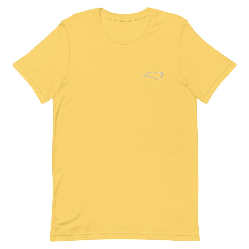 Puede incluir: Una camiseta amarilla de manga corta con un contorno blanco del estado de Carolina del Norte en el pecho izquierdo.