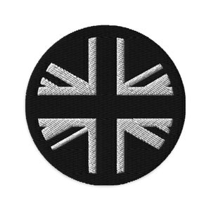 Puede incluir: Un parche bordado en blanco y negro con un diseño circular que presenta una bandera de la Unión Jack estilizada.