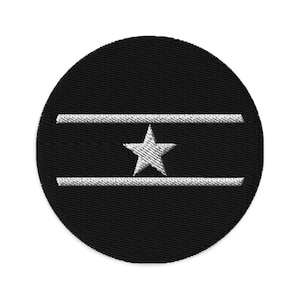 May include: A black circular patch with two white stripes and a white five-pointed star in the center.
