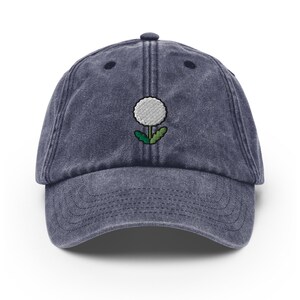 May include: A dark blue denim baseball cap with a white embroidered dandelion design.