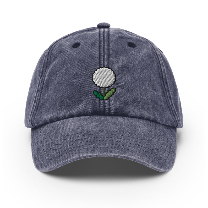 May include: A dark blue denim baseball cap with a white embroidered dandelion design.