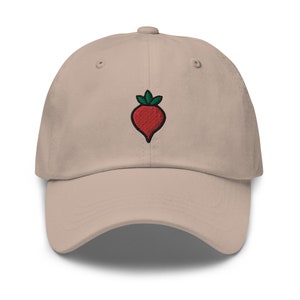 Puede incluir: Una gorra de béisbol beige con una remolacha roja bordada con hojas verdes.
