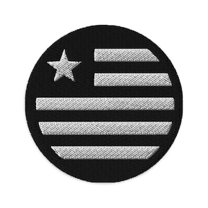 Può includere: Un cerotto circolare nero e bianco con una stella bianca e strisce che ricordano la bandiera americana.