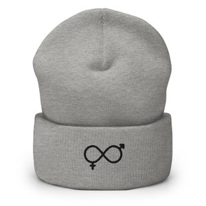 Könnte beinhalten: Hellgraue Beanie-Mütze mit umgeschlagenem Saum. Die Mütze zeigt ein schwarzes Unendlichkeitszeichen mit männlichen und weiblichen Geschlechtssymbolen. Die Mütze ist aus weichem Strickmaterial gefertigt.