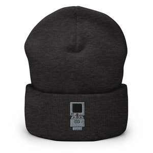 May include: A dark gray beanie with a gray and white embroidered image of a retro video game console with a joystick.