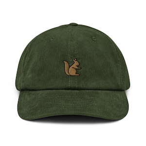 May include: A dark green corduroy baseball cap featuring a brown embroidered squirrel. The cap has a curved peak and an adjustable strap. The hat is a solid colour and has a classic, casual style. The cap is approximately 20 cm in diameter.