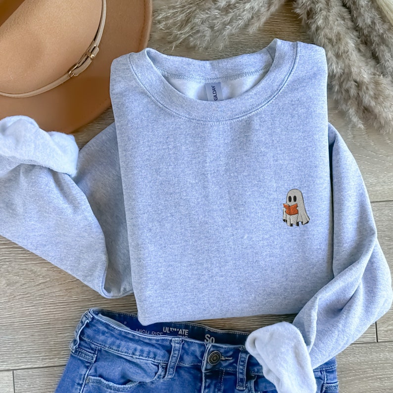 May include: A light gray sweatshirt with a small embroidered ghost holding a book. The ghost is white with black eyes and a red book.